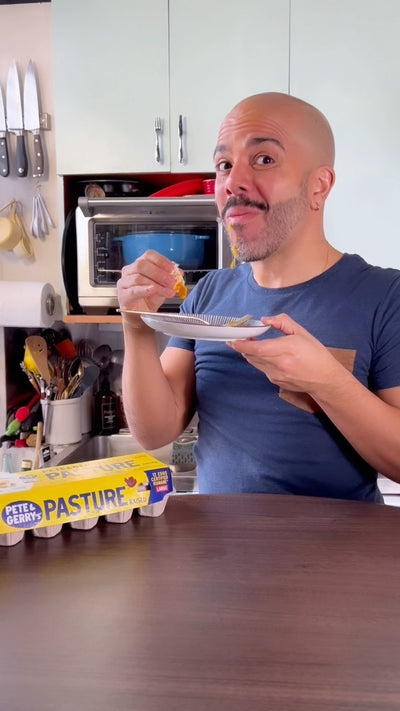 A man eating while sitting by a carton of Pete & Gerry's eggs