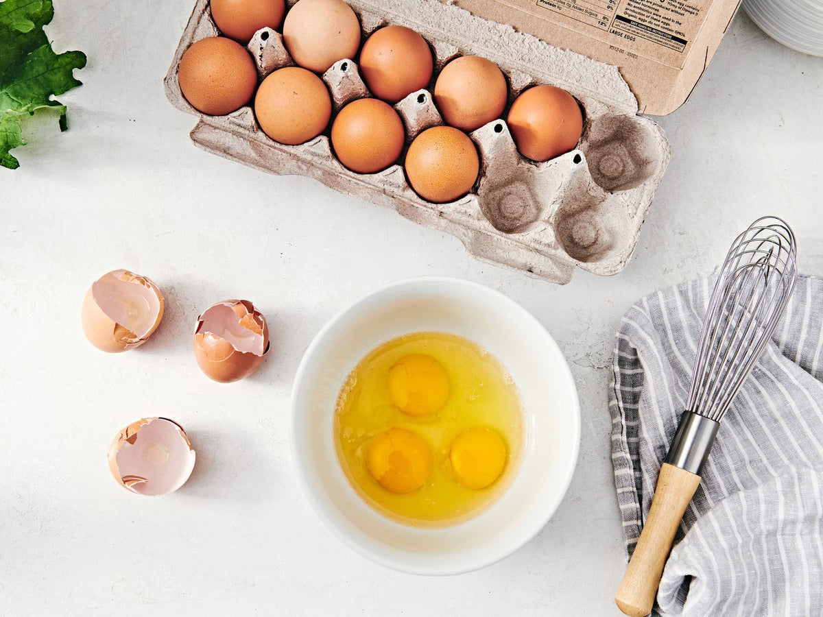 A carton of eggs, with three cracked into a bowl, ready to be whisked.
