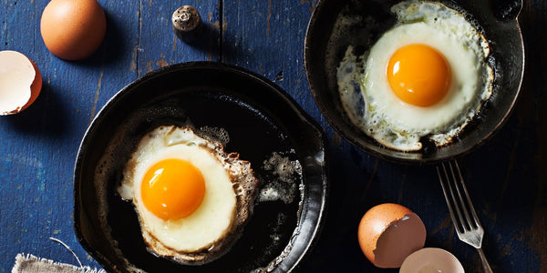 Two Pete & Gerry's eggs in miniature frying pans with vibrant golden yolks.