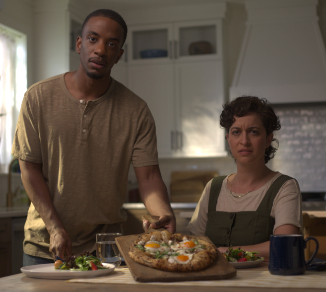 A man and woman eating a meal. They're both staring into the camera