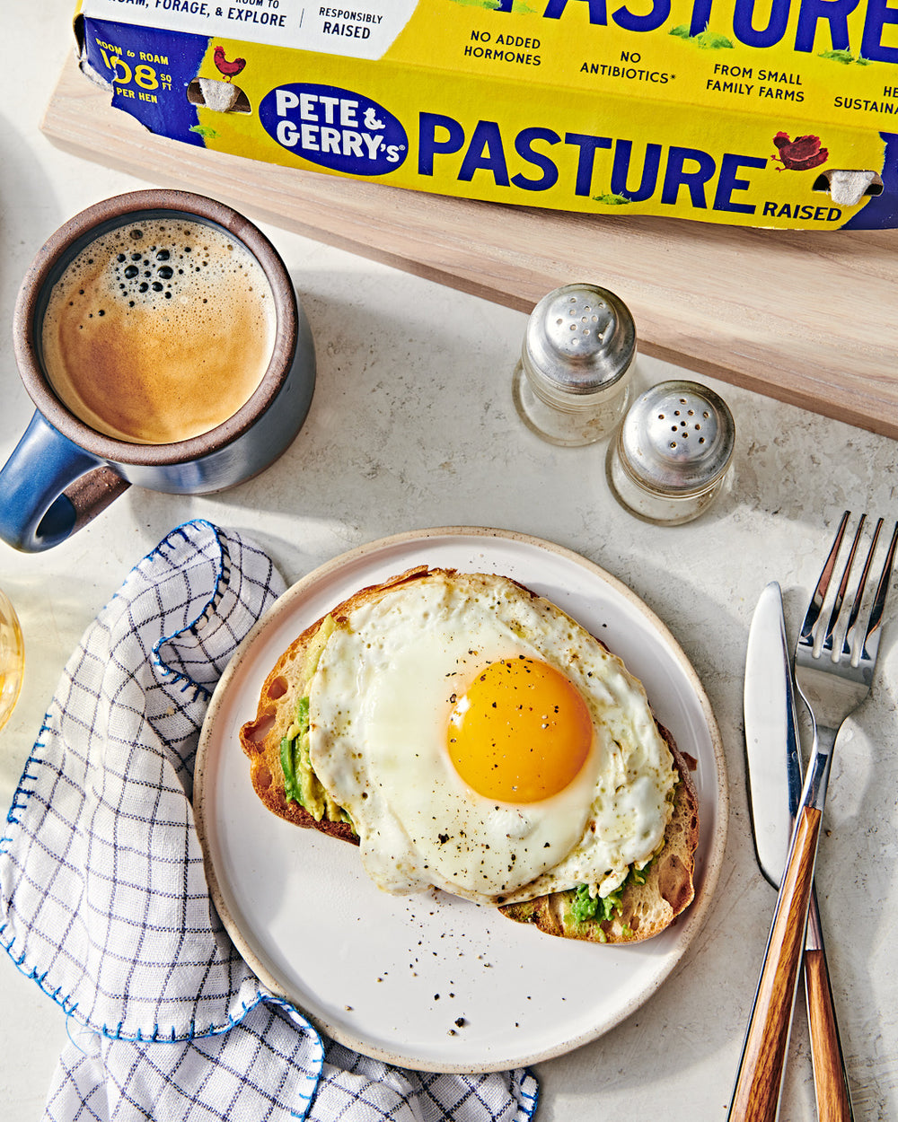 Sunny-side up eggs on toast by a carton of Pete & Gerry's eggs and a cup of coffee
