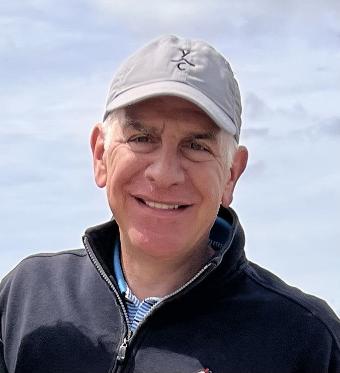 An older man smiling at the camera. He's wearing a baseball cap